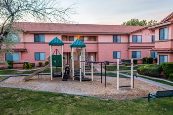 A playground with a slide and swings in front of a pink building.
